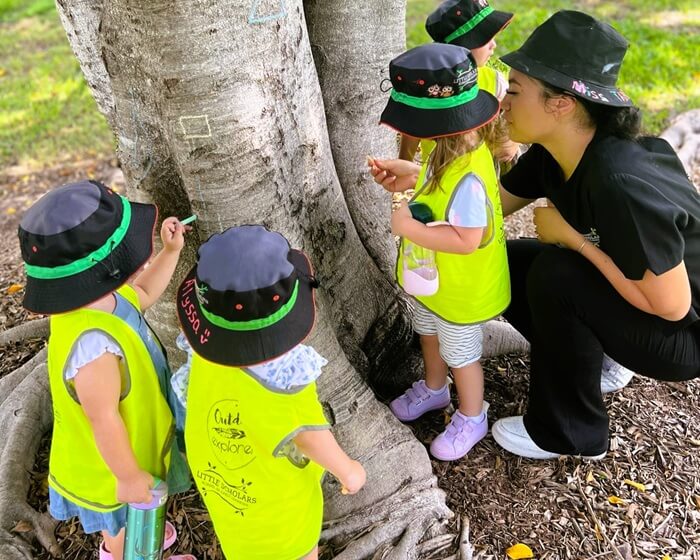 Little Scholars Educator And Three Children Drawing On A Tree Trunk During Outdoor Nature Exploration