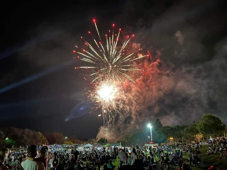 A vibrant fireworks display exploding high above a large crowd gathered in a park at night to celebrate Christmas on the Gold Coast.