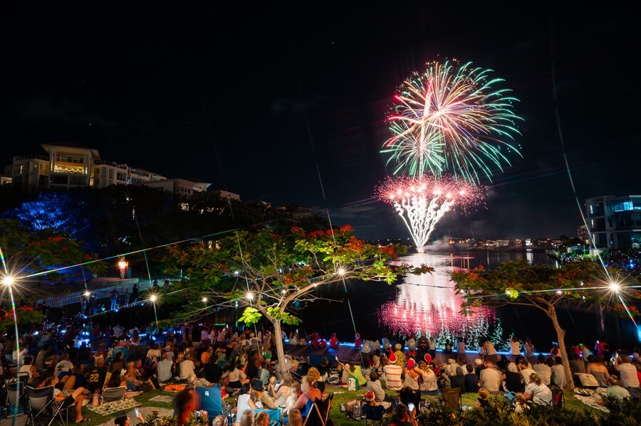 Spectacular fireworks reflecting over the water at night, with a large crowd gathered on the waterfront to watch the Christmas Gold Coast light show.