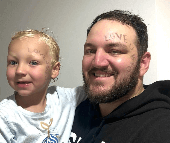 A smiling father and his young son from Little Scholars pose together, both featuring the phrase "LOVE U BRO" playfully written on their foreheads, capturing a fun and candid family moment.