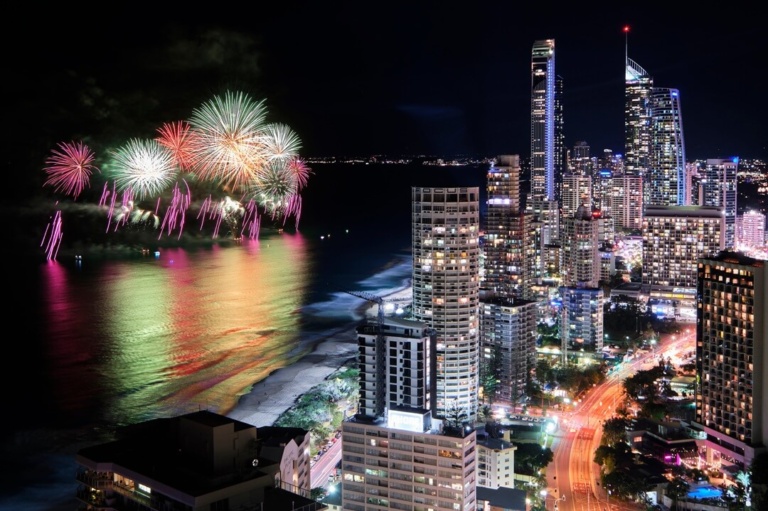 Vibrant fireworks display over the ocean next to the illuminated Gold Coast city skyline at night.
