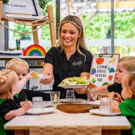An educator smiling while serving fresh fruit and vegetables to children during a mealtime activity at Little Scholars early learning centre.