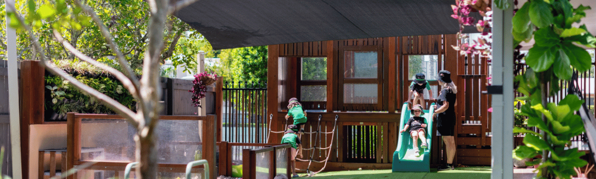 Children playing on slide outdoors with educator at Little Scholars