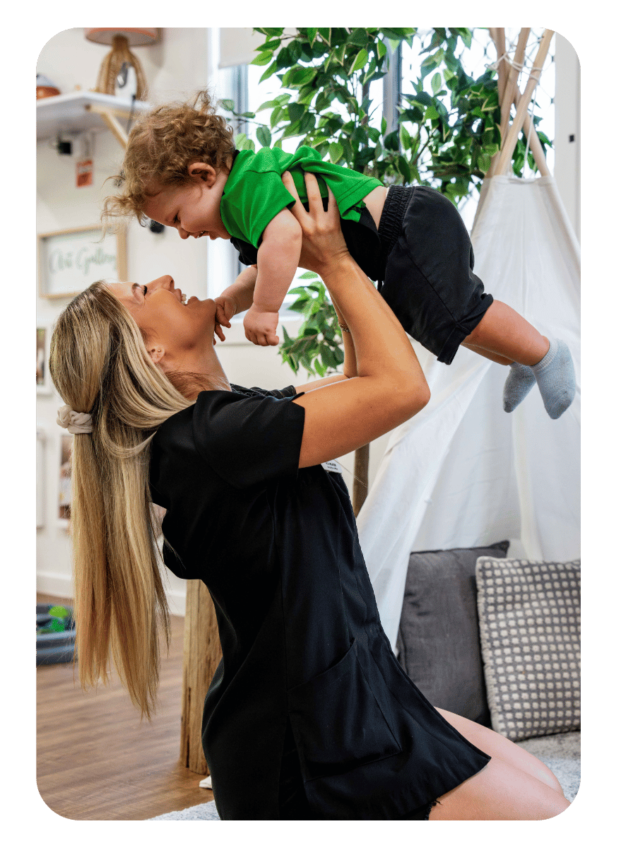 Little Scholars educator lifting and smiling with a baby in the nursery